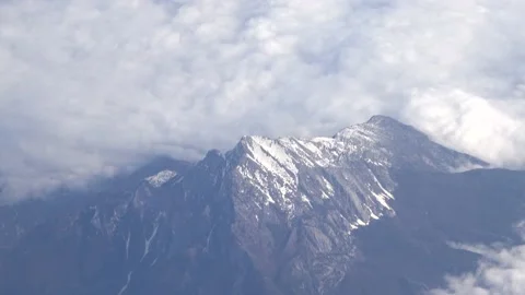 Flying over a snowy mountain surrounded by clouds 스톡 동영상 141560934
