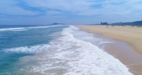Flying over the surf of the Indian Ocean above deserted beach on hazy day aer Stock Footage 87573952