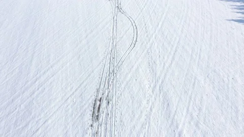 Flying over tire trails and foot steps in snow 4K drone video Stock Footage 101011283