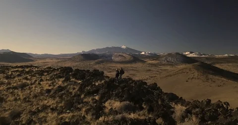 Flying over two men standing on the rim of a desert volcanic crater Stock Footage 106483164