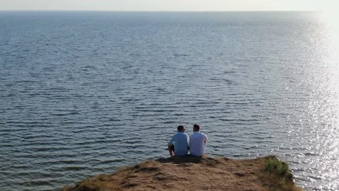 Flying over two men, who sits and speaks at the end of deep rocky abyss and sea Stock Footage 153310102