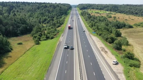Flying over a two-way road between forests and fields along which many cars Stock Footage 155320825