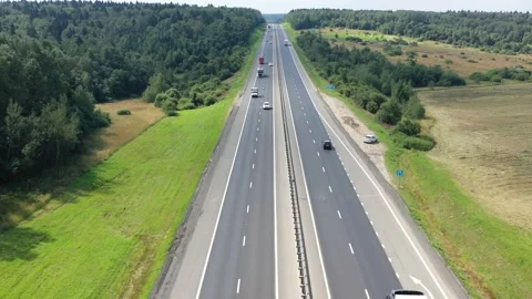 Flying over a two-way road between forests and fields along which many cars Stock Footage 156624783