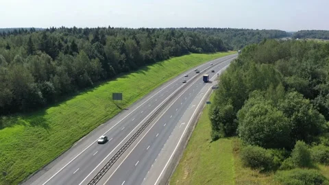 Flying over a two-way road between forests and fields along which many cars Stock Footage 157965500