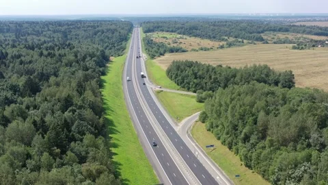 Flying over a two-way road between forests and fields along which many cars Stock Footage 159154079