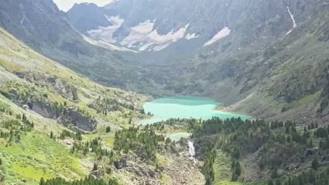 Flying over the waterfall and turquoise lake among the forest and mountains to t Stock Footage 264510894