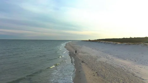 Flying over white beach at sunset with female jogger running along the shoreline Stock Footage 153268995