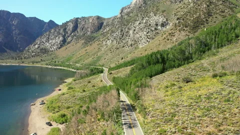 Flying over a windy road alongside a lake and a mountain range Stock Footage 143065463