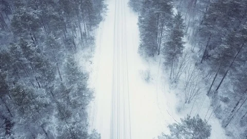 Flying over the winter forest and empty snow-covered road. It is snowing, frozen Stock Footage 101701302