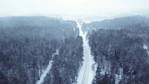 Flying over the winter forest and empty snow-covered road. It is snowing, frozen Stock Footage 101701585