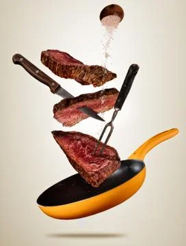 Flying pieces of beef steaks from pan on colored background. Foto stock