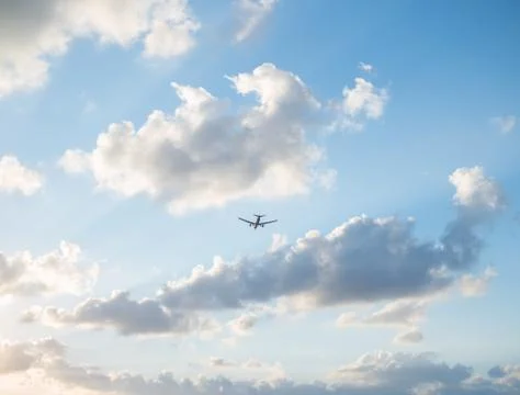 Flying plane in the sky with clouds at sunset as a background Stock Photos