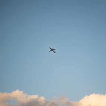 Flying plane in the sky with clouds at sunset as a background Stockfoto's