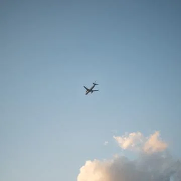Flying plane in the sky with clouds at sunset as a background Stock Photos