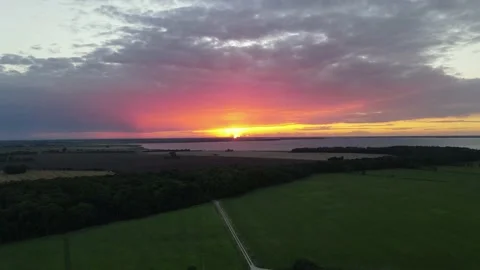 Flying Into Red and Yellow Cloudy Sunset With Green Fields and Sea, Baltic Sea Stock Footage