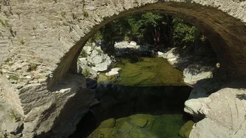 Flying through the arches of a stone bridge beside a shallow river, Corsica Stock Footage 85598128
