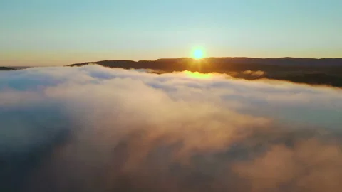 Flying through clouds to mountain range on horizon, sun shining, morning sunrise Stock Footage 141123142