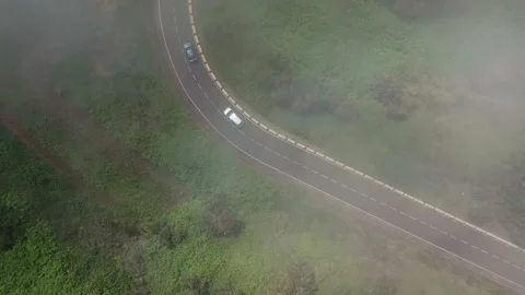 Flying through the clouds over a mountain road surrounded by green vegetation Stock Footage 139761246