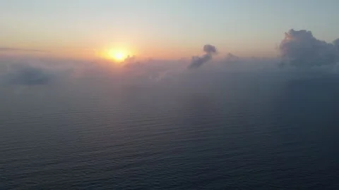 Flying through clouds over the sea, the camera captures the sunrise as it b.. Video stock 284872557