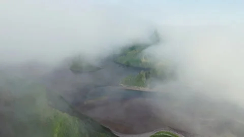 Flying through white clouds over dark sea with green hills at deserted shoreline Stock Footage 169093179