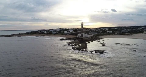 Flying towards lighthouse and touristic village at rocky peninsula at sunset 스톡 동영상 119090786