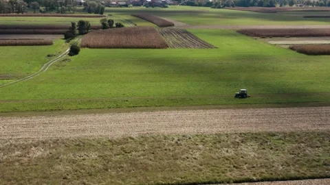 Flying towards lone tractor drives across vast green fields. Stock Footage 285772673