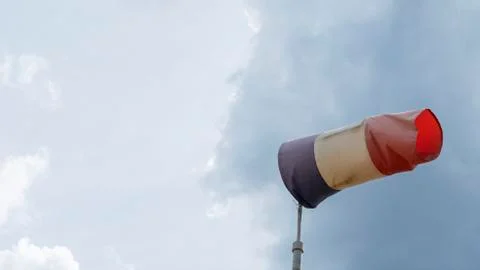 Flying windsock wind vane with red, white and blue lines on dramatic sky back Stock Photos