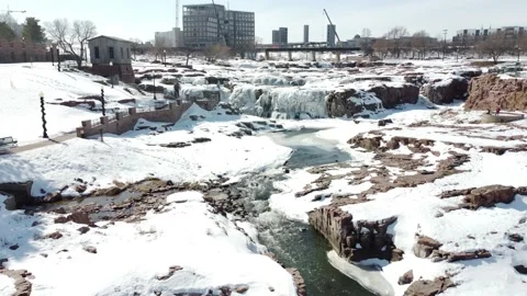 Flyover drone view of Sioux Falls Park with snow and ice covering the waterfall Stock Footage 234674599