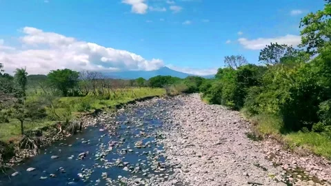 Flyover of Rocky River with Lush Greenery and distant blue Mountain Stock Footage 320496360