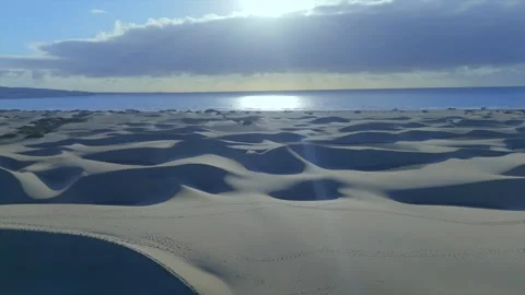 Flyover of Sand Dunes with Evening Sun Reflecting on Distant Ocean Stock Footage 310017849