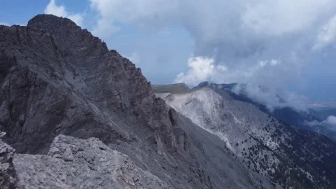 Flyover of two hikers standing at the edge of a mountain peak of Mount Olympus Stock Footage 239095035