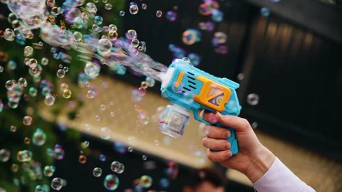 Foam bubbles fly out of a plastic toy gun. Shooting in slow motion Stock Footage 320556544