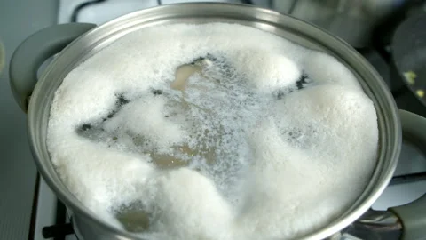 Foam forming on surface of boiling water in pot cooked on gas stove on kitchen. Stock Footage 312450600