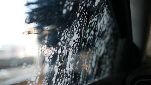 Foam streams flow down the windshield of the car in the car wash Stock Footage 129709073