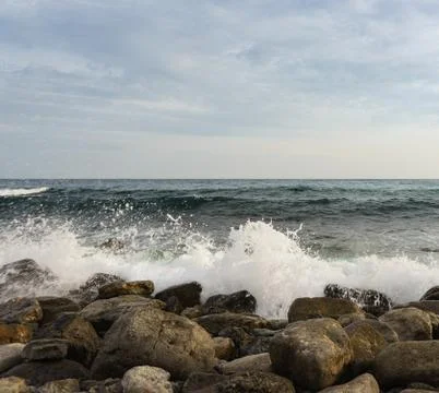 Foam waves break on large rocks on the shore. Evening Stock Photos