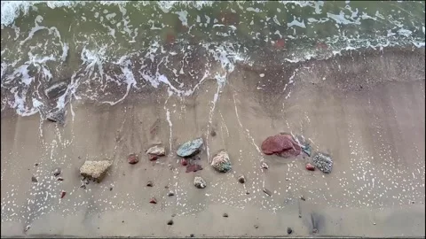 Foam waves wash over a sandy beach with small rocks. Stock Footage 320767491