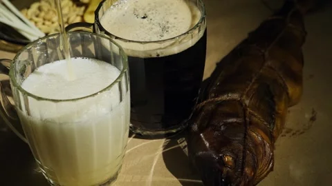 Foaming dark and light beer poured in mugs and fresh smoked fish, close-up. Stock Footage 258813145