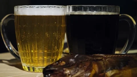 Foaming dark and light beer poured in mugs and fresh smoked fish, close-up. Stock-Footage 258813176