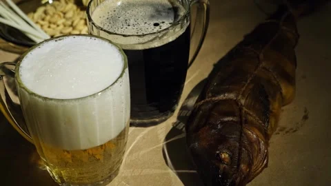 Foaming dark and light beer poured in mugs and fresh smoked fish, close-up. Video stock 260207454