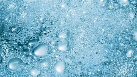 Foaming liquid soap texture. Blue bubbles background Stock Photos