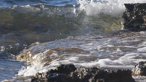 Foaming ocean waves crash dynamically over wet jagged coastal rocks Stock Footage 337415821