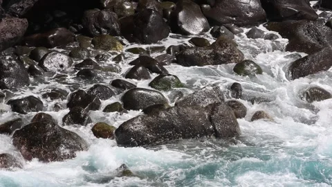 Foaming ocean waves crashing on dark smooth volcanic rocks Stock Footage 333602513