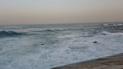 Foaming sea waves break and splash over rocky shallows near the concrete Stock Footage 345688339
