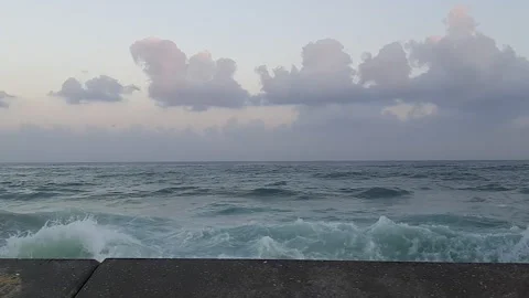 Foaming sea waves break and splash over rocky shallows near the concrete Stock Footage 345688568