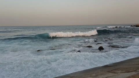 Foaming sea waves break and splash over rocky shallows near the concrete Stock Footage 345688600