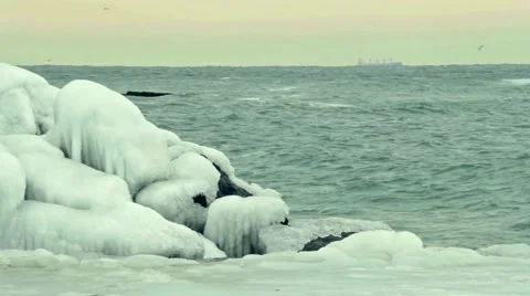 Foaming wave is breaking on the ice coverd stone. Cargo container ship sailing. 스톡 동영상 55425044