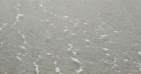 A foaming wave rolls over a sandy seashore and retreats glittering in the sun Stock Footage 154406910