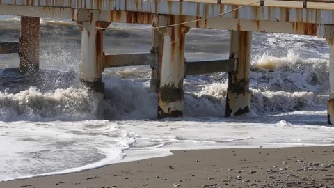 Foaming waves crashes on rusty metal pier on a sandy sea shore. Handheld shot Stock Footage 79092332
