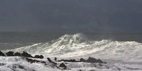 Foaming waves exploding across a dark reef with Hawaii's coastal hills in Stock Footage 59525575