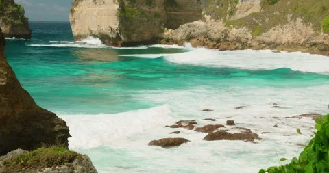 Foaming white waves break against dark coastal rocks in a tropical Indonesian Stock Footage 344756401